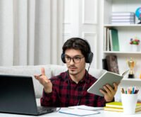 Student attending virtual class with headphones, laptop, and study materials in a home office setup.