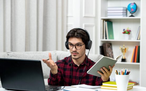 Student attending virtual class with headphones, laptop, and study materials in a home office setup.