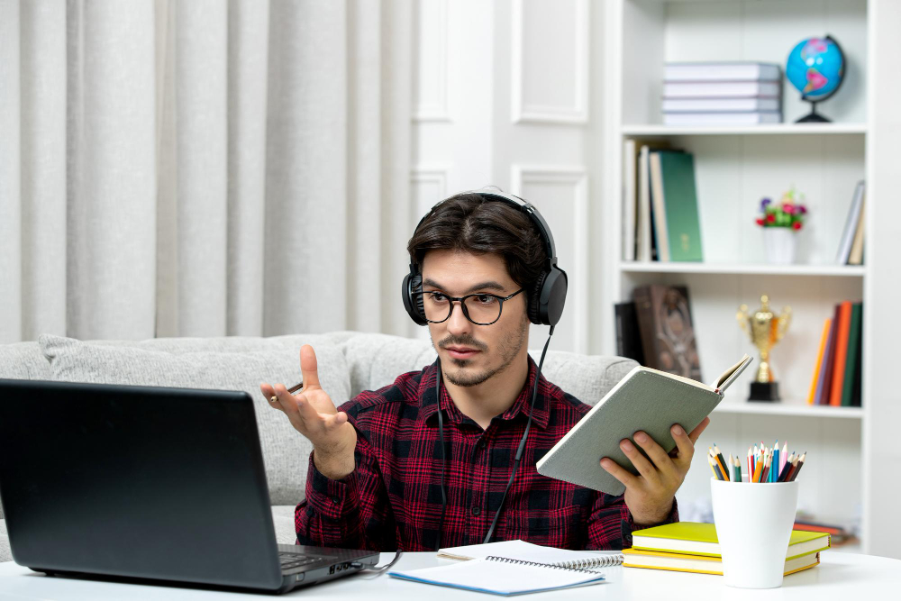 Student attending virtual class with headphones, laptop, and study materials in a home office setup.