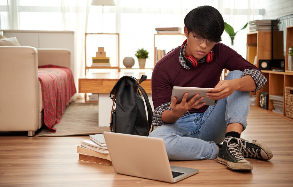 Young student studying online with tablet and laptop at home, representing remote learning and digital education