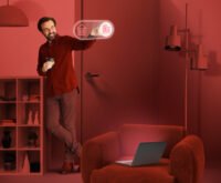 Man interacting with futuristic smart home interface while standing in a red-toned modern living room with a laptop on an armchair