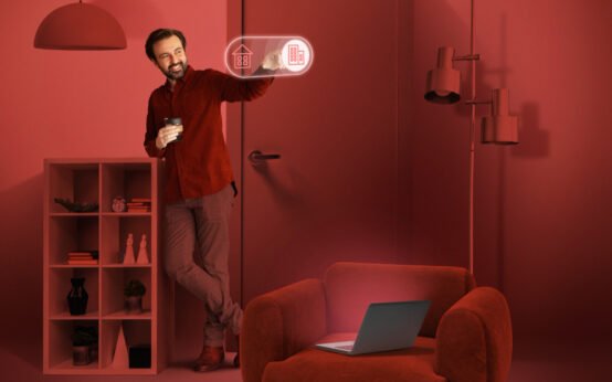 Man interacting with futuristic smart home interface while standing in a red-toned modern living room with a laptop on an armchair
