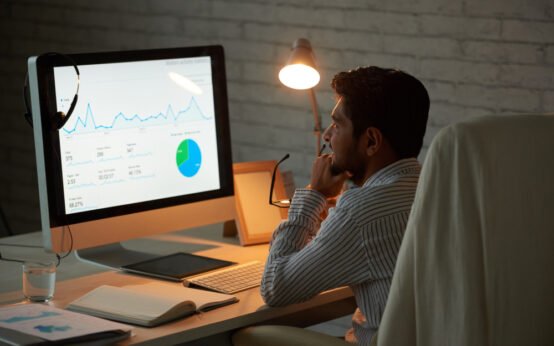 Business analyst reviewing financial performance graphs and pie chart on desktop monitor in low-light office environment