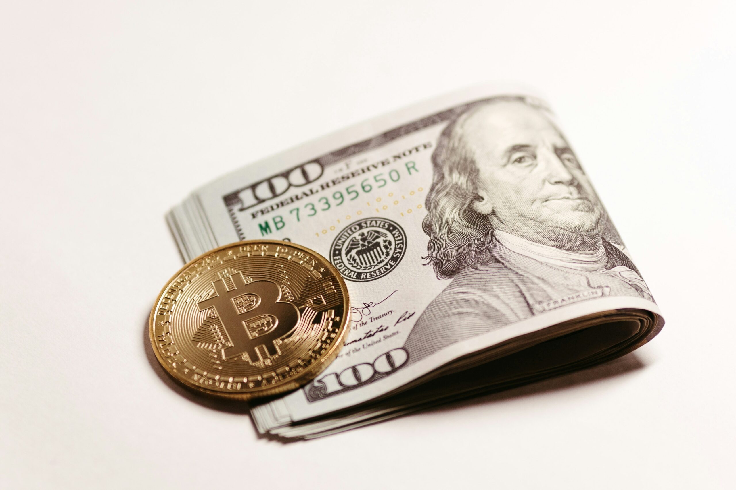 Gold Bitcoin coin placed next to a stack of folded US hundred-dollar bills