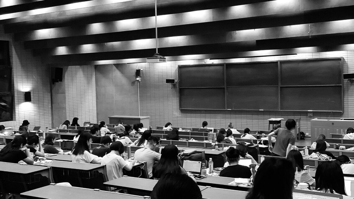 University students studying in a modern lecture hall with laptops and notebooks during a classroom session.