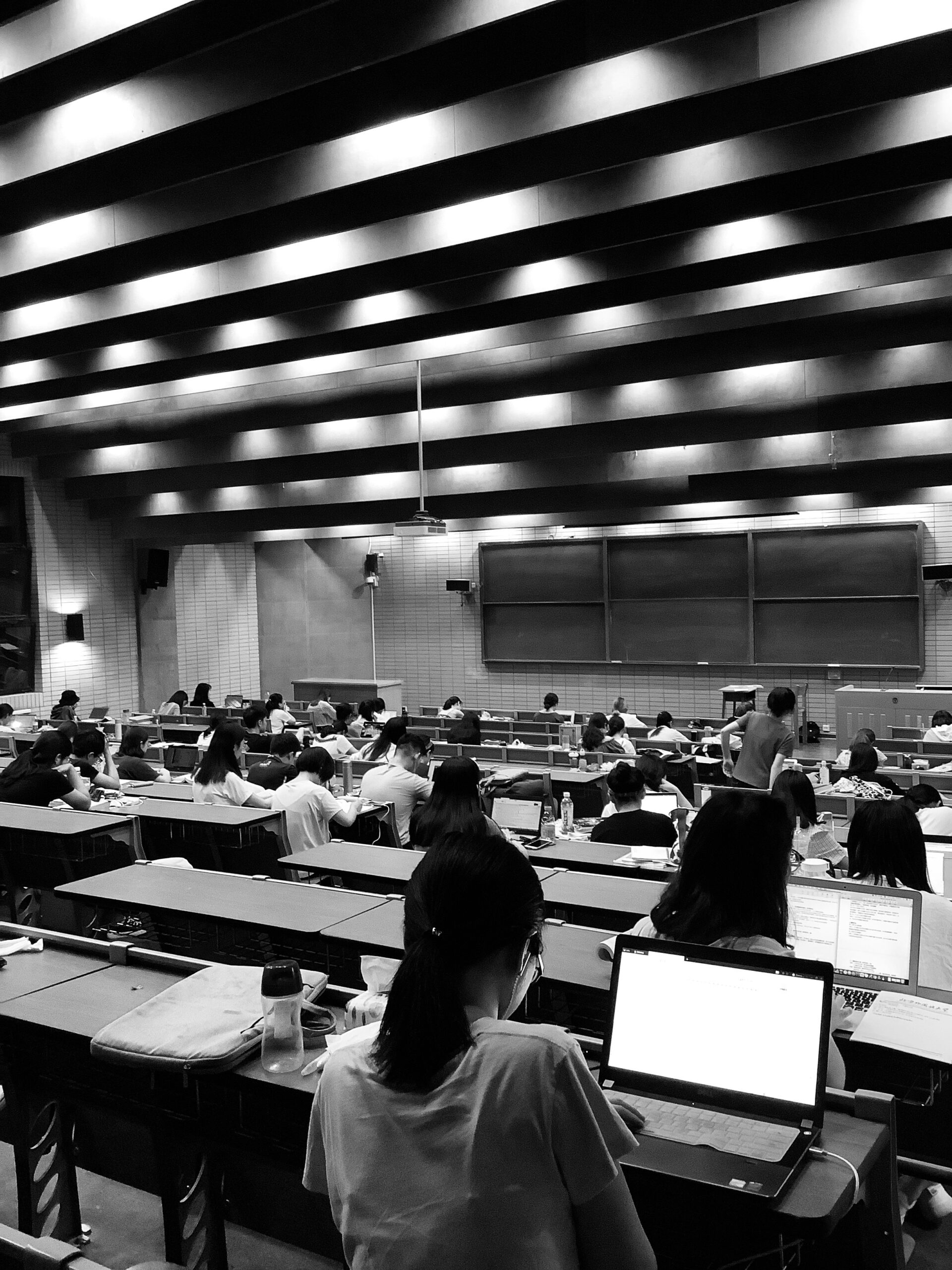 University students studying in a modern lecture hall with laptops and notebooks during a classroom session.