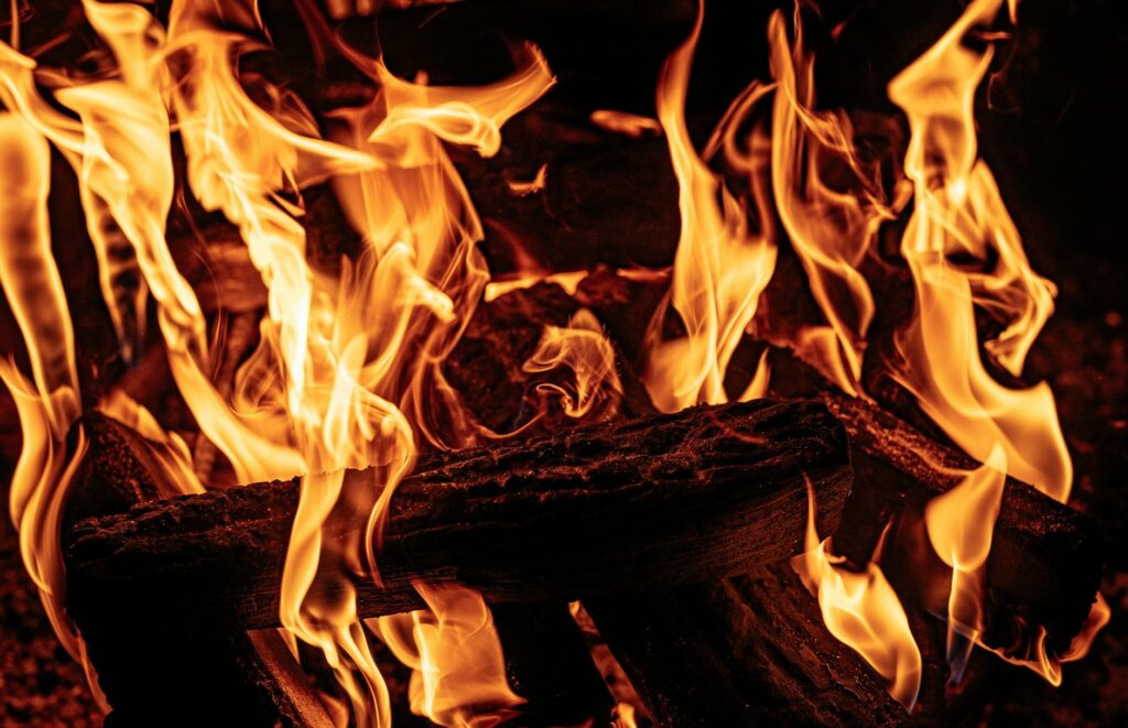 A detailed close-up shot of vibrant orange and yellow flames dancing in a beach fire pit at night.
