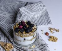 A white bowl filled with creamy Greek yogurt, topped with fresh blueberries, raspberries, and a sprinkle of golden granola, illustrating a probiotic-rich breakfast.