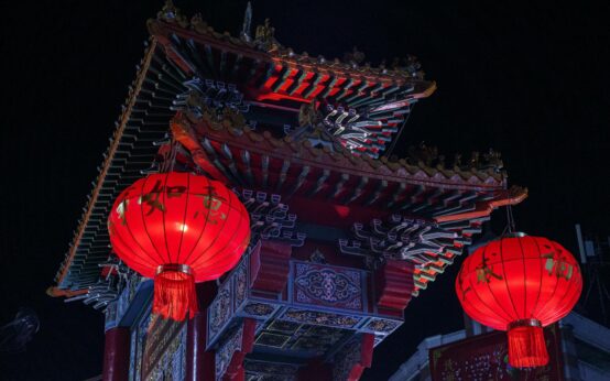 A traditional wooden boat drifts down a Suzhou canal illuminated by glowing red lanterns at dusk.