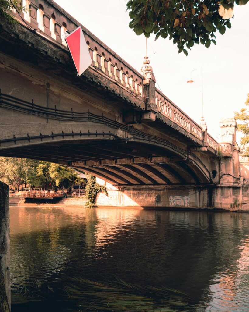 An ancient, arched stone bridge reflected in the still, green water of a tranquil Suzhou canal.