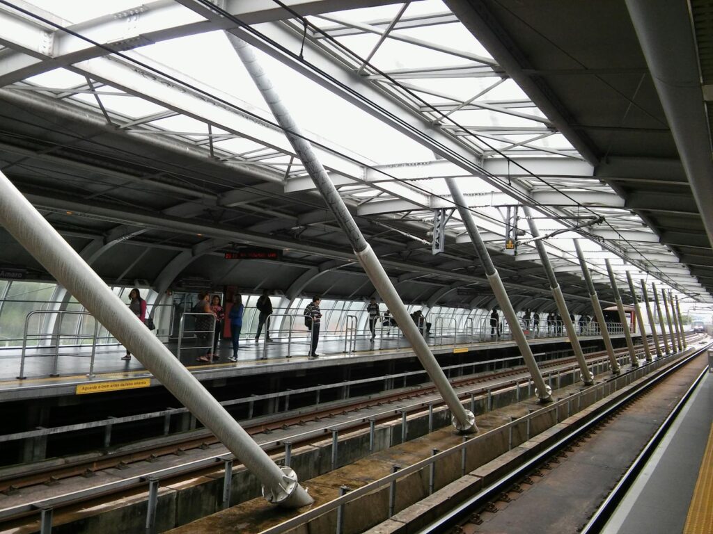 A diverse group of commuters standing behind the yellow line on an immaculately clean Singapore MRT station platform.