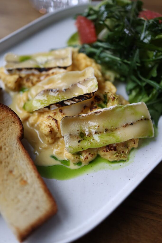 A smiling woman taking a bite of a large, healthy salad in a white bowl, filled with vibrant greens, cherry tomatoes, and sliced avocado.