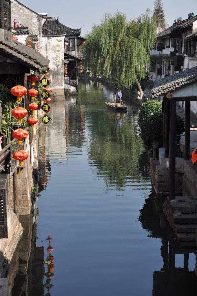 A local woman walks along the historic Pingjiang Road in Suzhou, with whitewashed buildings and traditional wooden balconies lining the canal.