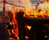 A group of friends laughing around a warm bonfire on a sandy beach as the sun sets over the ocean.