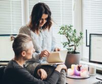 A woman smiling while working on her laptop at a clean, modern home office desk.