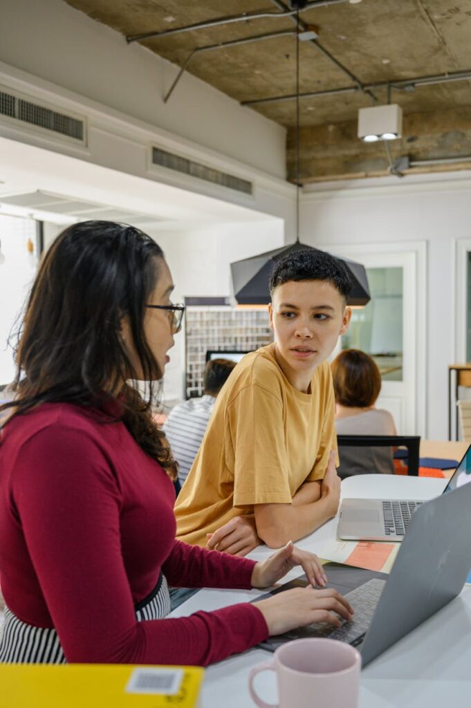 A side view of a modern humanoid robot and a female engineer collaborating at a desk with multiple computer screens.