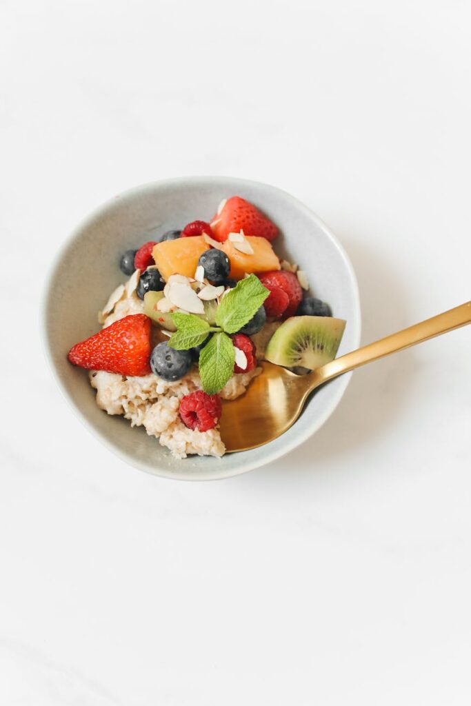 A close-up shot of a white bowl filled with oatmeal, topped with fresh blueberries, strawberries, and sliced bananas.