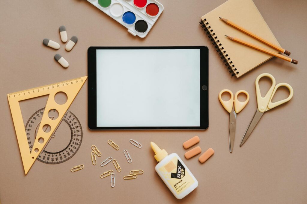 An overhead shot of a digital creator's desk with a tablet displaying a design, a notebook, and a pen.