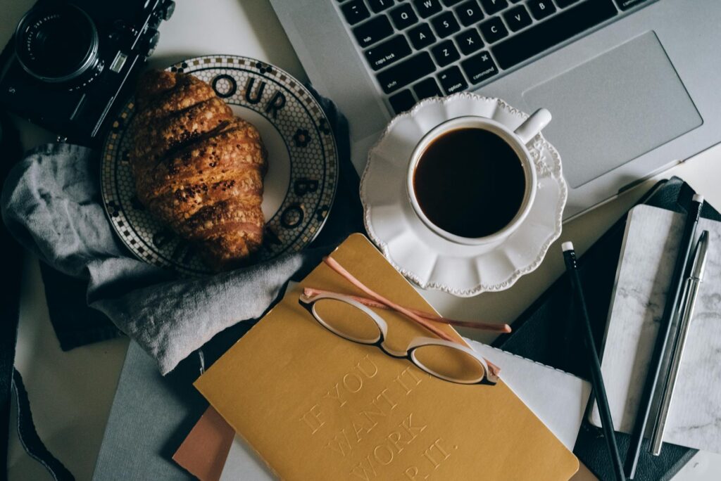 An overhead shot of a desk with a laptop, design sketches, and a cup of coffee, representing creative online work.