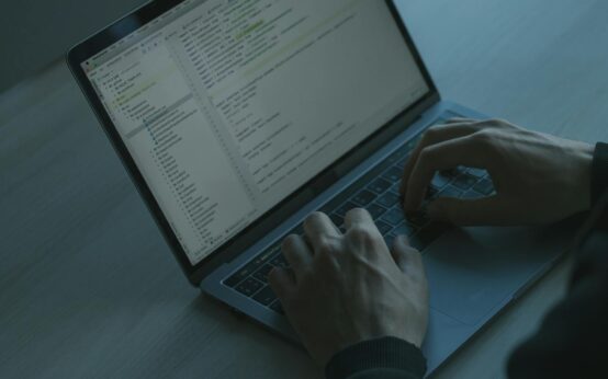 A hooded figure representing a hacker types code on a laptop, illustrating DeFi security risks.