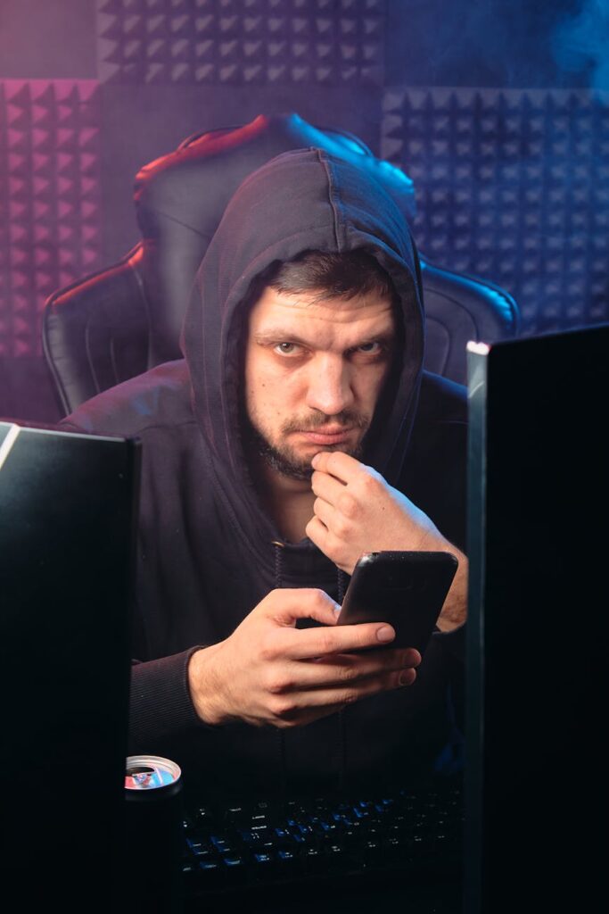 A silhouette of a person in a hoodie in front of a computer screen with cascading green binary code, representing a cyber threat.