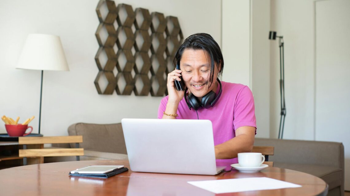 A freelancer comfortably working on their laptop at a sunlit wooden desk in their home office.