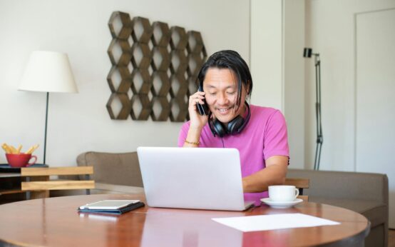 A freelancer comfortably working on their laptop at a sunlit wooden desk in their home office.