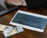 A laptop on a wooden desk with a stack of cash next to it, symbolizing making money online.