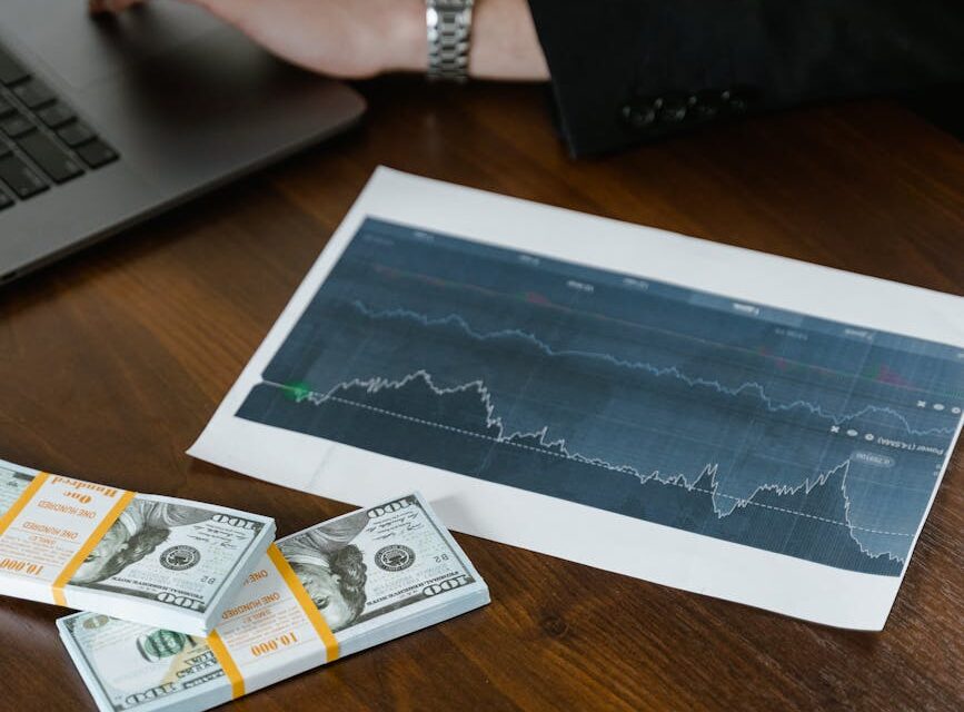 A laptop on a wooden desk with a stack of cash next to it, symbolizing making money online.