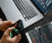 A freelance web developer's desk with a laptop displaying code, a smartphone, and cash.