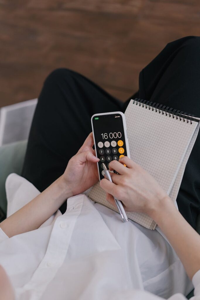 A modern smartphone lying on a wooden desk next to a neat stack of hundred-dollar bills.