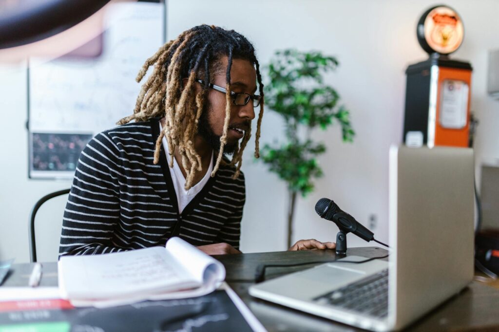 A focused entrepreneur wearing headphones, smiling as they edit their podcast audio on a laptop in a cozy home office.