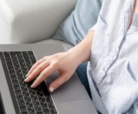 A woman smiling while typing on her laptop at a clean, modern home office desk.