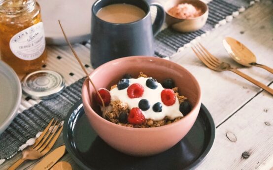 A close-up of a white ceramic bowl filled with creamy Greek yogurt, topped with fresh blueberries, raspberries, and crunchy granola.
