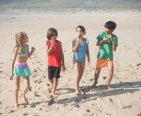 A happy multi-generational family with grandparents, parents, and children walking and laughing together on a sunny beach.