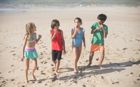 A happy multi-generational family with grandparents, parents, and children walking and laughing together on a sunny beach.