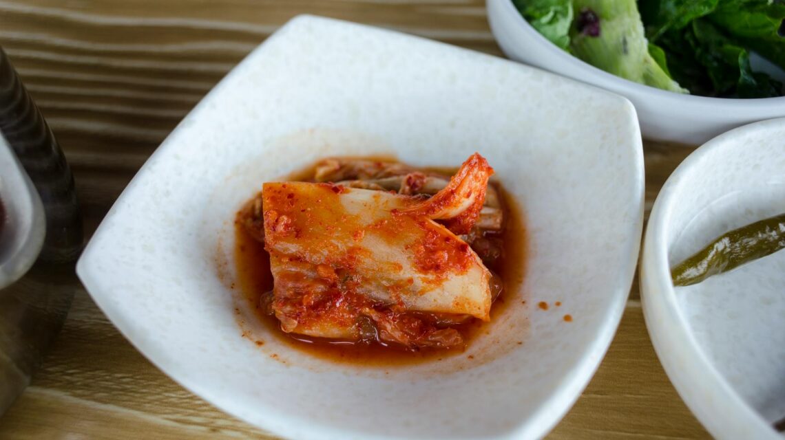 An overhead shot of various fermented foods, including vibrant red kimchi and pale sauerkraut, in ceramic bowls, showcasing sources of probiotics.