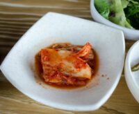 An overhead shot of various fermented foods, including vibrant red kimchi and pale sauerkraut, in ceramic bowls, showcasing sources of probiotics.