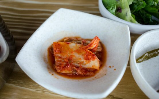 An overhead shot of various fermented foods, including vibrant red kimchi and pale sauerkraut, in ceramic bowls, showcasing sources of probiotics.