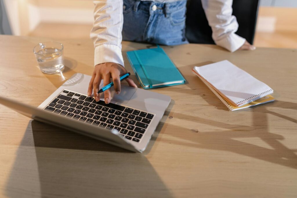 Close-up of hands typing on a laptop, symbolizing earning money online as a virtual assistant, with a small piggy bank nearby.
