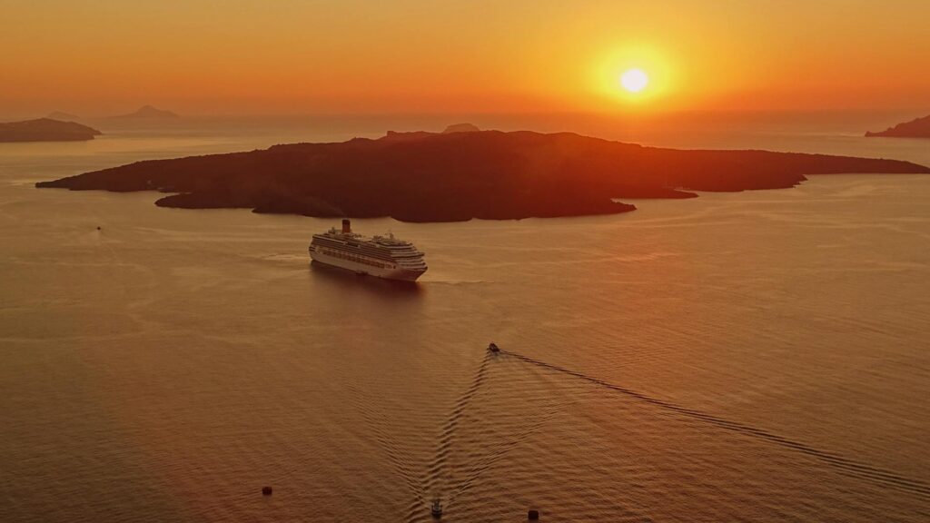 A silhouette of a couple holding hands while watching the vibrant sunset from a clifftop in Santorini.