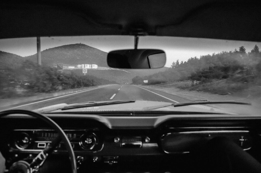 View from inside a car, showing the dashboard and a scenic mountain highway stretching ahead.