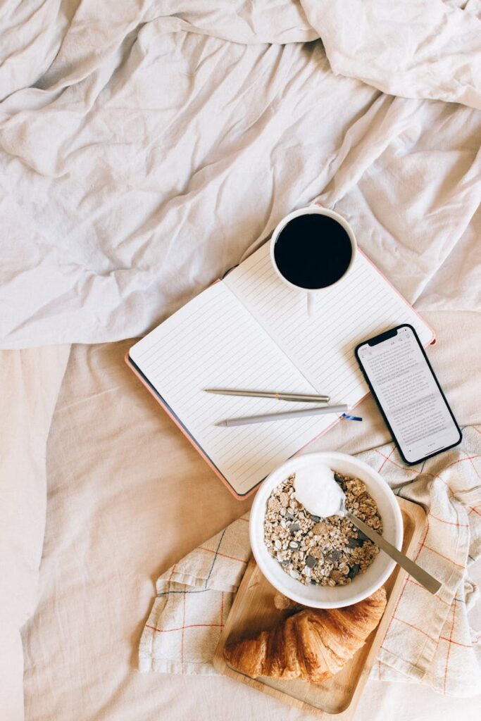 A person's hands writing in a leather-bound travel journal next to a steaming cup of coffee and a map.