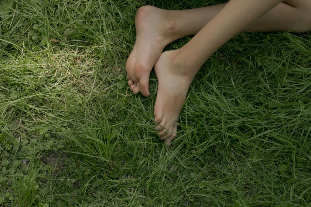 Top-down view of bare feet in green grass with a hand holding a green smoothie.