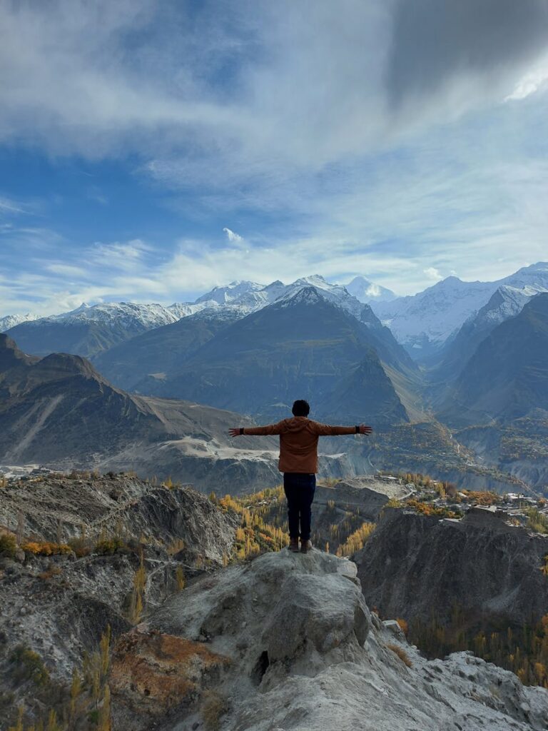 A person sitting on a rock overlooking a vast mountain range, writing in a travel journal.