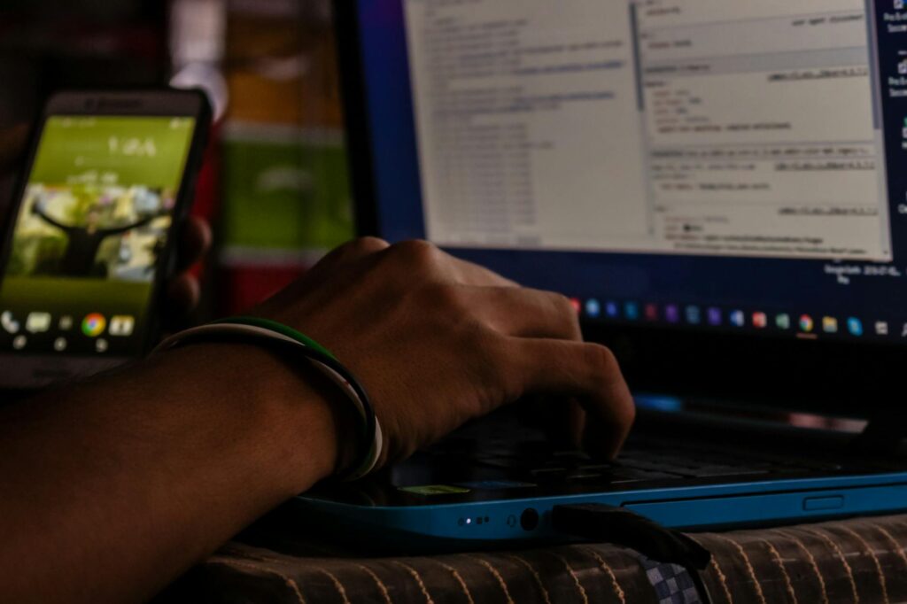 A detailed shot of a student's hands typing complex code on a laptop keyboard in a computer lab.