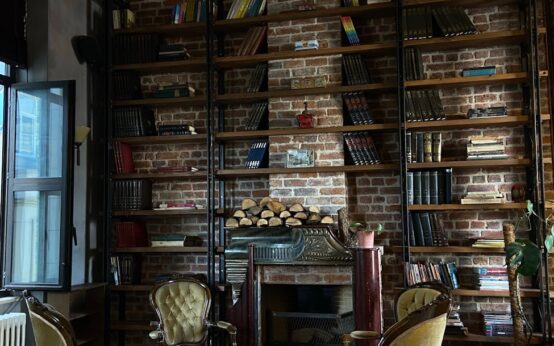 A comfortable armchair sits next to a warm fireplace in a hotel library filled with books.