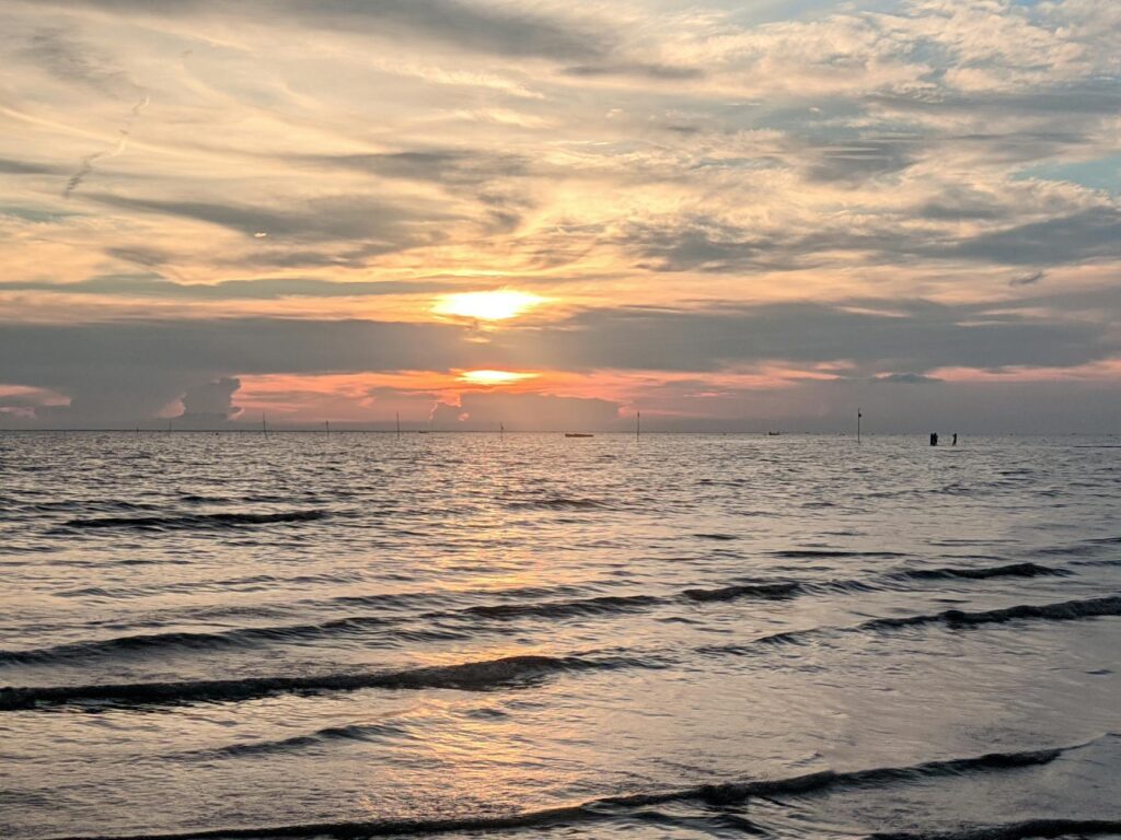 An airplane wing cuts across a stunning view of puffy cumulus clouds and a deep blue sky from a passenger window.