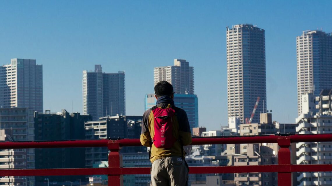 A traveler in a casual jacket looks down at a paper map while standing on a city street.