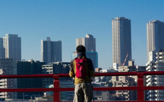 A traveler in a casual jacket looks down at a paper map while standing on a city street.